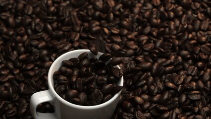 Close up of coffee bean falling in to coffee cup surrounded by pile of beans. Dropping aromatic blending bean in to white cup. Top view of coffee drop in to glass with black background. Comestible.