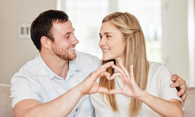 Happy, hands in heart and couple on sofa for bonding, loving relationship and relax in home. Marriage, emoji and man and woman with hand sign on couch for love, affection and care in living room