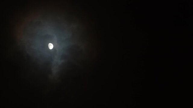 The Moon in the dark night sky is surrounded by glowing clouds. Moonlight on a cloudy night. Natural background and free space for text