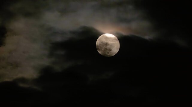 Supermoon in dark clouds. Full moon in the night cloudy sky close-up