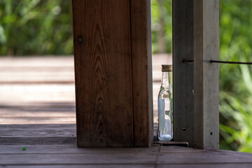 empty liquor bottle rests hidden behind a pier wall, evoking a sense of abandonment and mystery. The juxtaposition of nature and human presence tells a story of leisure and neglect