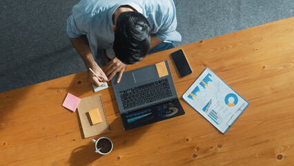 Skilled businessman writing idea on colorful sticky notes while looking at data analysis. Caucasian project manager working on laptop while taking a note in sticky notes at meeting room. Convocation.