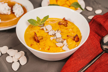 Vegetable soup, pumpkin and carrot puree with seeds, mushrooms, chanterelles and mint in a white bowl on a gray background with a burgundy napkin and a black spoon