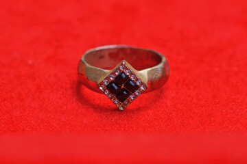 one yellow gold ring with purple stones lies on the red table