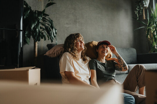 Happy lesbian couple having fun while sitting near sofa during relocation