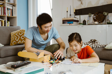 Siblings helping each other while assembling science project at home