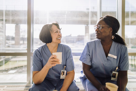 Smiling senior female doctor holding glass while talking with colleague during coffee break at hospital
