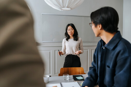 Female entrepreneur explaining ideas to colleagues in meeting room while standing in front of transparent wipe board at