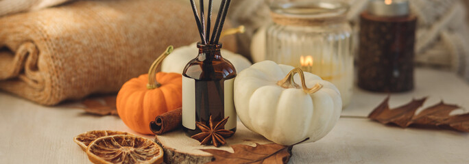 Aroma diffuser, pumpkins, dry citrus, candles on wooden tray, knitted warm plaid. Fall hygge home decor, aromatherapy. Copy space, banner white. Autumn cozy mood composition on the windowsill