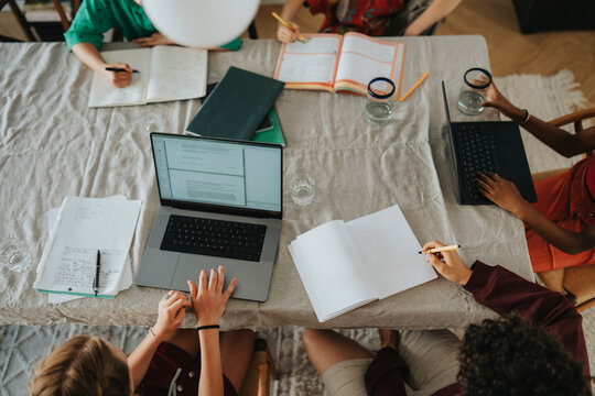 High angle view of group of friends doing homework and using laptop while sitting near table at home