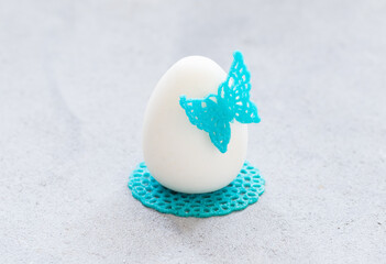 Obraz premium Mousse Cream chocolate cake in the shape of an Easter egg, decorated with blue waffle lace decor, with a butterfly and a napkin.