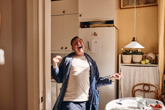 Cheerful mature man listening to music while standing in kitchen at home