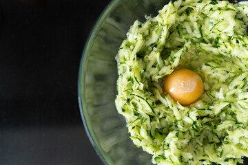 A cracked egg with zucchini in a bowl, ready for making healthy waffles. For culinary, healthy eating, cooking, or recipe content.