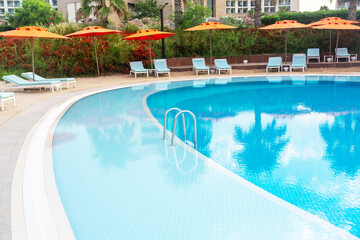 Step into a luxurious pool with a strip of coastal sand and brightly colored umbrellas and sun loungers