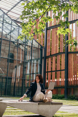 Woman working outdoors on laptop in modern office atrium, blending nature and technology