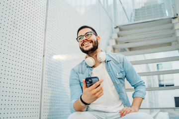 Young caucasian man student listening to music while sitting on stairs