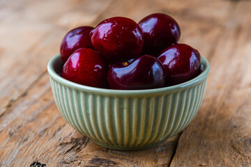 Ripe cherries in a ceramic green bowl on a wooden background. Minimalism.