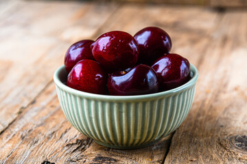 Ripe cherries in a ceramic green bowl on a wooden background. Minimalism.