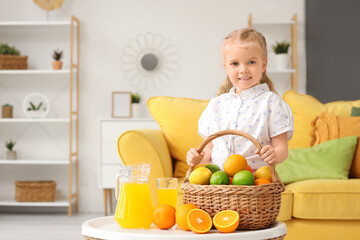 Cute little girl with basket of citrus fruits and juice on table at home