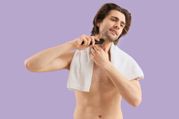 Naklejka premium Young man trimming his beard on lilac background