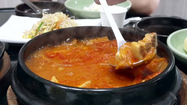 팔팔 끓고 있는 한국의 푸짐한 돼지고기 두부 김치찌개와 덜어내는 모습