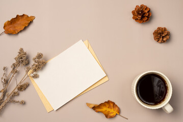 Paper blank sheet with leaves, cone and cup of coffee on beige background from above. Autumn composition. Space for text