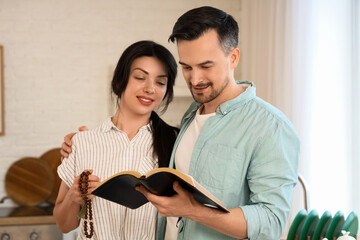 Religious couple with praying beads reading Holy Bible in kitchen