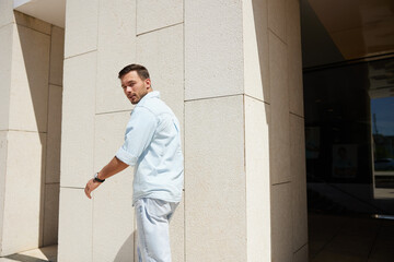 Young man in casual attire walking past a modern building, glancing back with a curious expression