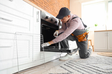 Male technician repairing electric oven in kitchen