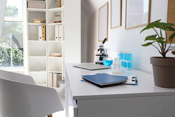 Laptop with chemical glassware and microscope on desk in laboratory