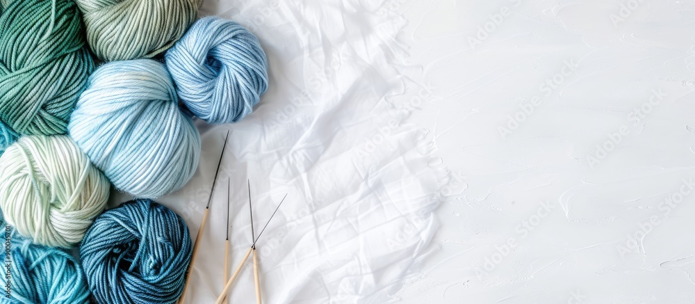 Poster a bird s eye view of blue and green yarn with knitting needles on a white backdrop with ample copy s