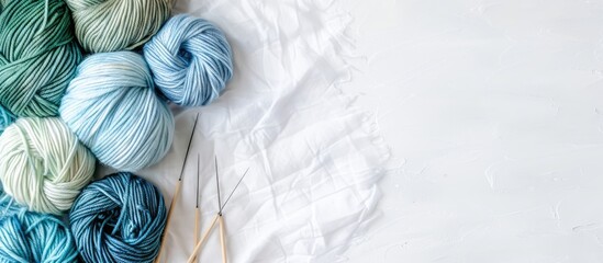 A bird s eye view of blue and green yarn with knitting needles on a white backdrop with ample copy space image provided