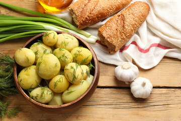Tasty young boiled potatoes in bowl served on wooden table, flat lay