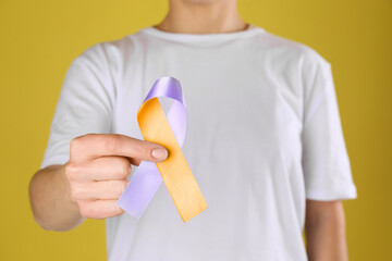 World Psoriasis Day. Woman with orange and orchid ribbon as symbol of support on yellow background, closeup