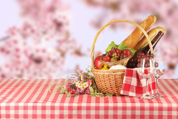 Picnic basket with foods and wine on table in nature. Space for text