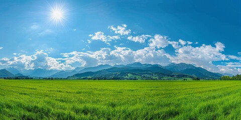 Obraz premium Breathtaking Panoramic Natural Landscape: Lush Green Meadow Under Vibrant Blue Sky with Fluffy Clouds and Majestic Mountains. Idyllic Scenery Perfect for Relaxation, Outdoor Adventure, and Environment