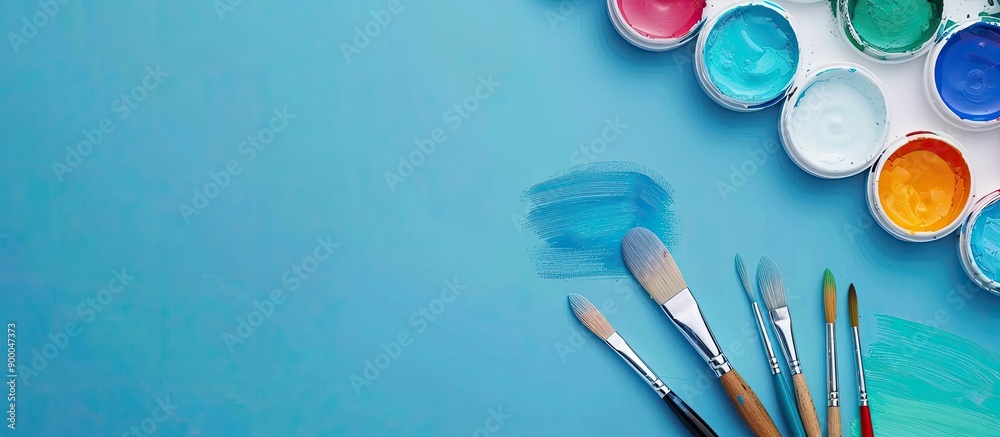Poster close up of watercolor paints and brushes on a blue background with copy space image available