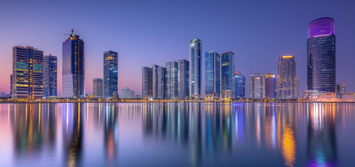 Obraz premium A vibrant city skyline at dusk, with illuminated skyscrapers reflecting beautifully on the calm water