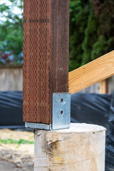 New house construction in residential neighborhood, closeup job site detail, round foundation cement pouring form with metal bracket and wood 4x4 beam installed
