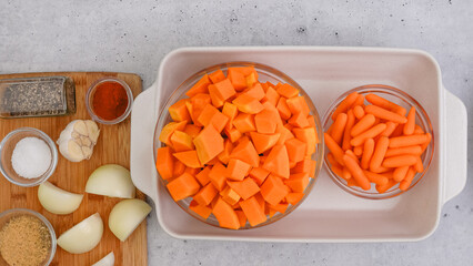 Roasted butternut squash soup recipe. Peeled and seedless squash cubes, carrot, onion, garlic, and spices close-up in a ceramic baking dish