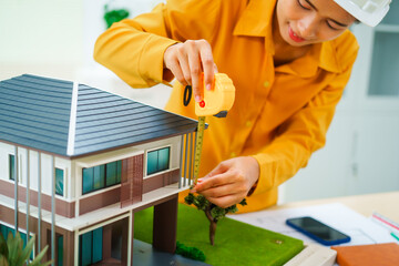 Fototapeta premium An Asian female architect analyzes blueprints at her desk in the office. She specializes in house design, focusing on roofs and walls, and collaborates with construction contractors in her company.
