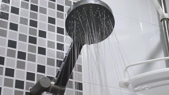 Shower head, flowing water in bathroom. Bottom view of holes in shower head built into. Water flows pouring down from shower head. Using water, taking bath, douche, showering