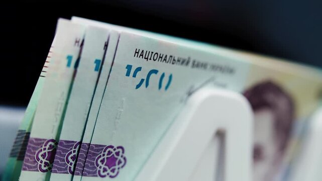 Close up of money counting machine counting thousand of hryvnia banknotes for currency exchange, payment or investment. Automatic bill counter. Ukrainian money bills. Finance and banking concept.