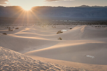 Sun burst over the mountains on Mesquite Dunes in Death Valley, CA