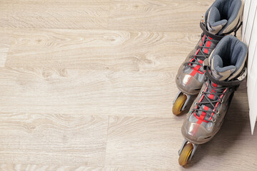 Old roller skates with cloth shoe and plastic base near radiator on wood floor with rubber wheels....