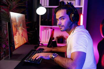 Smart gaming streamer enjoy playing battle team with streaming online shooting gun game with multi or single player at warship on pc screen, wearing headset at digital neon light cyber room. Surmise.