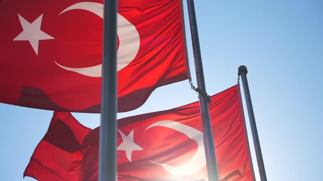 Slow motion of the row of Turkey national flags on high flagpole waving in the wind against the sun and clear blue sky