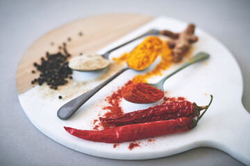 Board, spices and spoon in gray background for curry, flavor and sensory appeal for creativity with culinary. Studio, condiment and seasoning for cooking with powder, aroma and ingredients collection