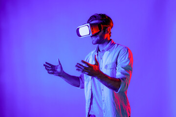 Side view of happy man holding and moving gesture while using VR goggle. Happy person using headset and goggle while enter virtual world or metaverse with neon light background. Technology. Deviation.