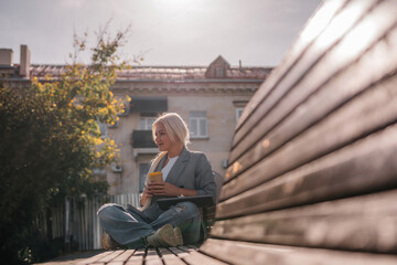 A woman sitting on a bench with a cell phone in her hand. She is wearing a suit and she is working on her phone.